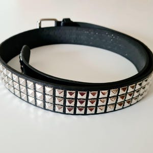 May include: Black belt with two rows of silver pyramid studs. The belt features a silver buckle and a textured leather finish. A classic accessory for adding a touch of edge to any outfit.