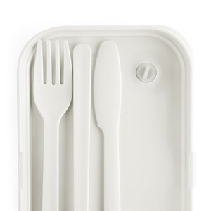 Puede incluir: Una fiambrera de pl&aacute;stico blanco con un tenedor, cuchillo y cuchara integrados. La fiambrera tiene un cierre para mantenerla cerrada.