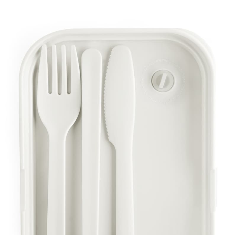 Puede incluir: Una fiambrera de pl&aacute;stico blanco con un tenedor, cuchillo y cuchara integrados. La fiambrera tiene un cierre para mantenerla cerrada.