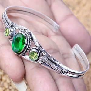 Op de afbeelding: Zilveren armband met een groene edelsteen en twee kleinere groene edelstenen. De armband heeft een ingewikkeld ontwerp.