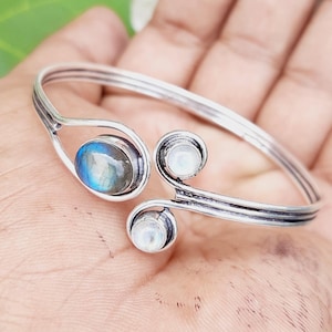 Op de afbeelding: Zilveren armband met drie edelsteen accenten. De middelste steen is een blauwgroene labradoriet, en de twee kleinere stenen zijn witte maansteen.