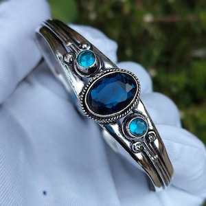 Puede incluir: Pulsera de plata con una gran piedra azul ovalada y dos piedras turquesas redondas más pequeñas.