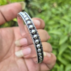 May include: A silver-toned metal cuff bracelet featuring a central row of polished spherical beads flanked by two twisted rope-style borders. The bracelet has an oxidized finish in the recessed areas to highlight the textured metal details.