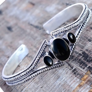 Puede incluir: Pulsera de plata con tres piedras ovaladas negras engastadas en un diseño decorativo.
