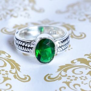 May include: A silver ring with a braided band and a large, oval-shaped green gemstone.