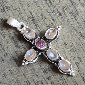 Puede incluir: Un colgante de cruz de plata con cinco piedras de luna ovaladas y una piedra rosa en el centro.