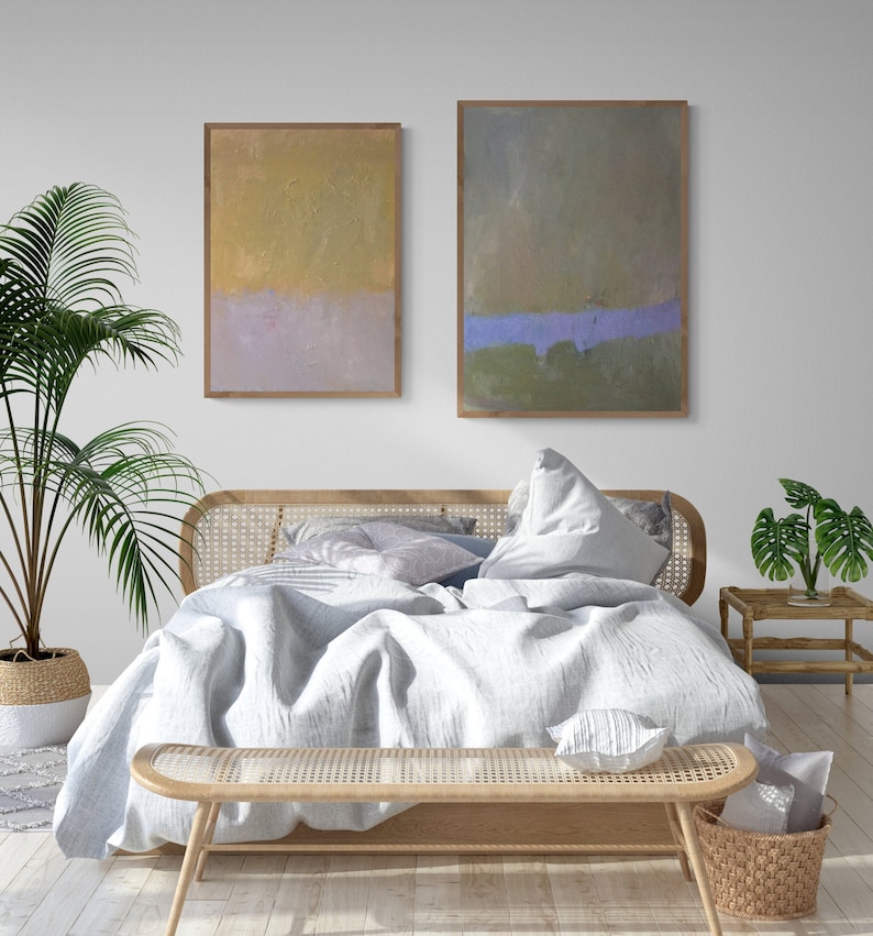 May include: A white linen bed with a wooden headboard and a matching wooden bench at the foot of the bed. Two abstract paintings hang on the wall behind the bed. A potted plant sits on the floor next to the bed.