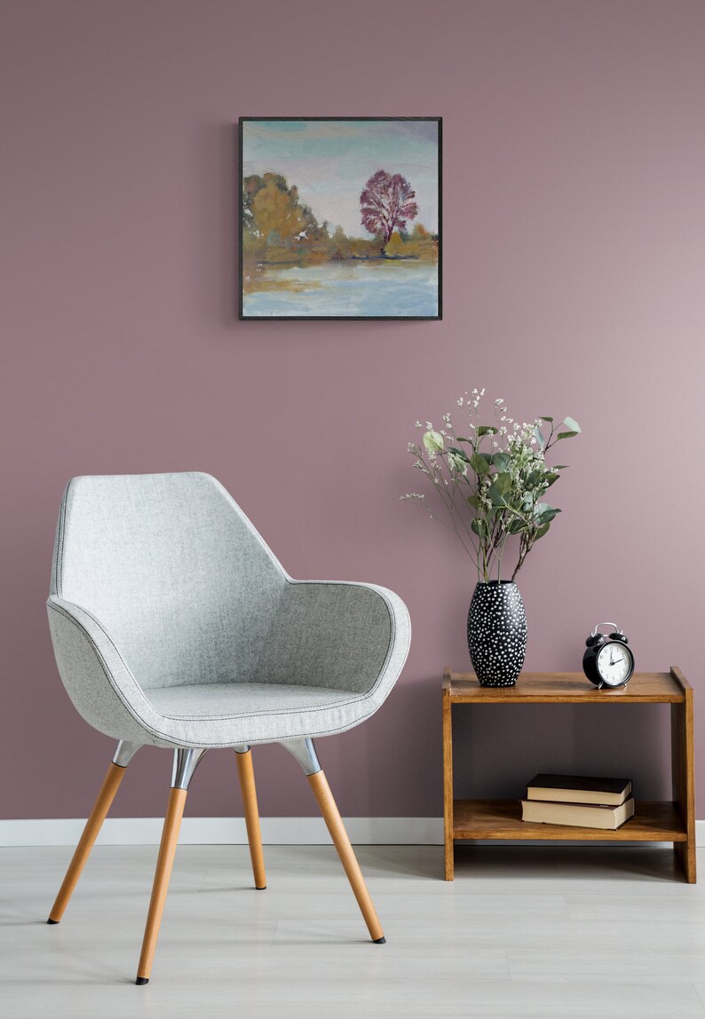 Puede incluir: Un sill&oacute;n gris tapizado con patas de madera se encuentra frente a una pared rosa. Una peque&ntilde;a mesa auxiliar de madera con un jarr&oacute;n de flores blanco y negro y un despertador negro se encuentra junto al sill&oacute;n. Un cuadro enmarcado de un paisaje con un &aacute;rbol rojo cuelga de la pared.
