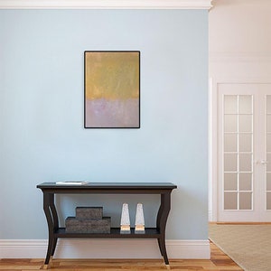 May include: A light blue wall with a framed abstract painting in gold and purple hues. A black console table with a shelf sits in front of the wall. The table has two decorative items on the shelf.