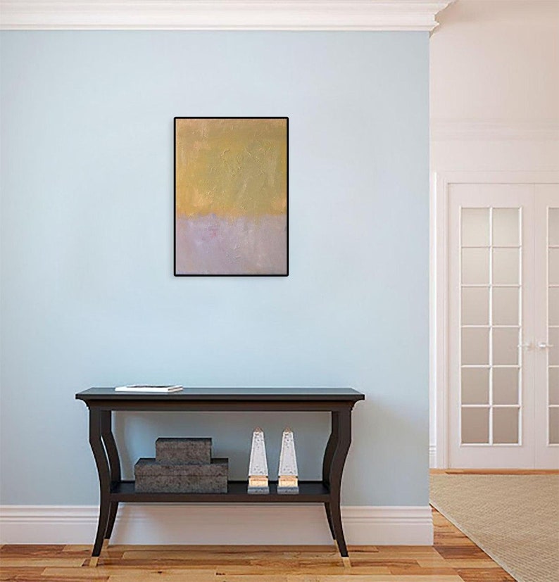 May include: A light blue wall with a framed abstract painting in gold and purple hues. A black console table with a shelf sits in front of the wall. The table has two decorative items on the shelf.