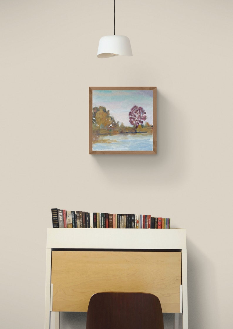 Puede incluir: Una pintura enmarcada de un paisaje con un solo &aacute;rbol rojo en el centro, rodeado de &aacute;rboles verdes y un lago azul. La pintura est&aacute; en un marco de madera y est&aacute; colgada en una pared blanca.