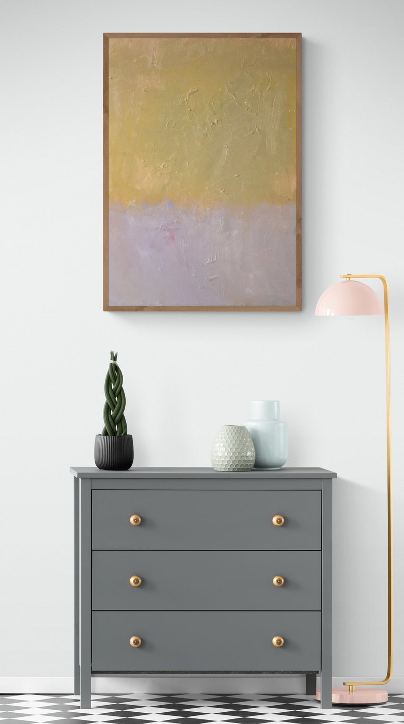 May include: A gray dresser with three drawers and gold knobs. The dresser is in front of a white wall with a framed abstract painting above it. There are two decorative vases and a potted plant on top of the dresser. A pink lamp with a gold base is on the right side of the image.