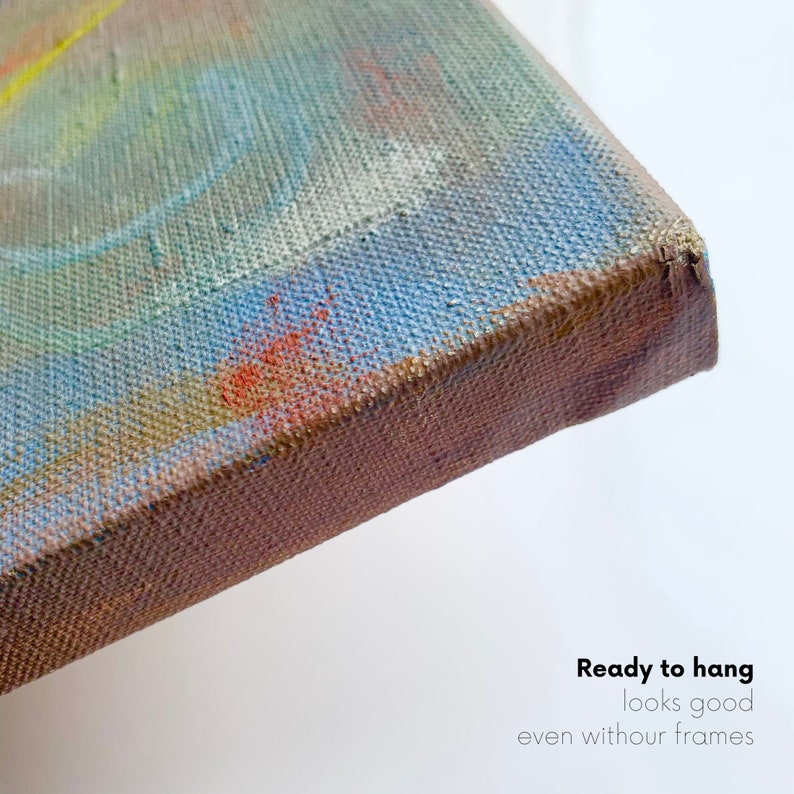 May include: Close-up of the edge of a canvas painting. The canvas is stretched over a wooden frame and the edges are painted a brown color. The painting is abstract with blue, green, yellow, and orange colors. The text "Ready to hang looks good even without frames" is visible at the bottom of the image.