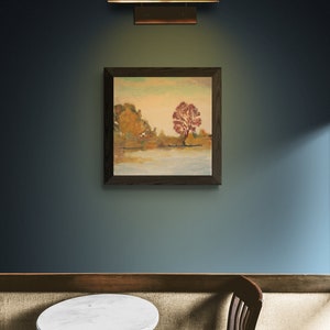 Puede incluir: Una pintura enmarcada de un paisaje con un &aacute;rbol rojo en el centro, colgada en una pared azul con una mesa y una silla de madera marr&oacute;n en primer plano.
