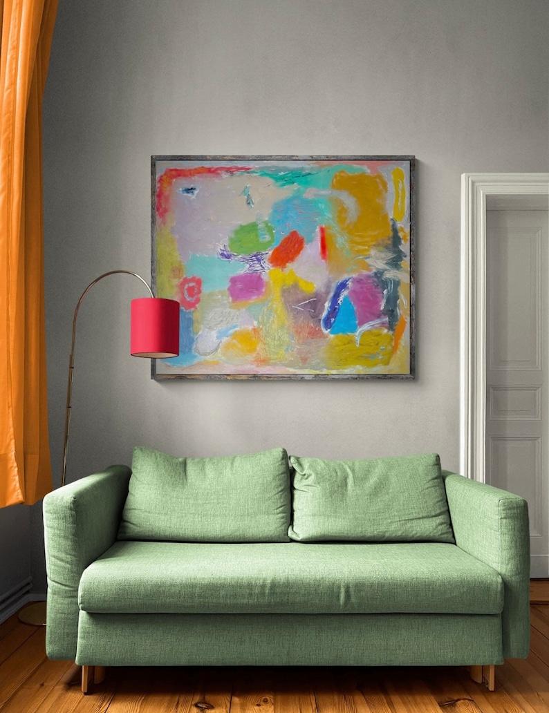 May include: Abstract painting with a colorful, textured design in shades of blue, green, yellow, pink, and orange. The painting is framed in a simple wooden frame and hangs on a light gray wall above a green sofa.