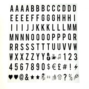 May include: A collection of black letter and symbol tiles on a white background. The tiles include the alphabet, numbers, and various symbols such as hearts, stars, and musical notes. The letters and numbers are in a bold, sans-serif font.