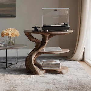 Può includere: Un tavolino in legno a tre livelli con un design unico e organico. Il ripiano superiore ospita un giradischi nero con una copertura trasparente. Il ripiano centrale contiene un disco, e il ripiano inferiore una pila di dischi.
