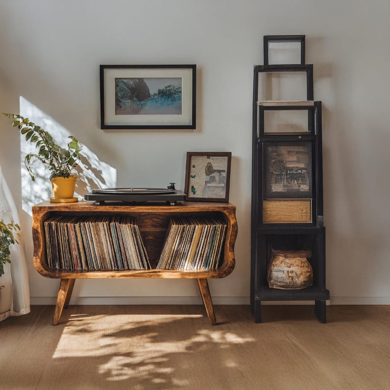May include: A wooden record player console with a curved front, holding vinyl records. A black record player sits on top, with a framed picture and a potted plant. A black framed shelf unit is to the right.
