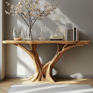 Puede incluir: Una consola de madera natural con una base única en forma de tronco de árbol. La mesa está adornada con objetos decorativos, incluyendo un jarrón con ramas, libros y un candelabro. El diseño de la mesa añade un toque natural a cualquier espacio habitable.