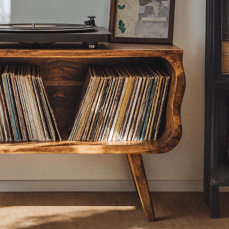May include: A wooden record player console with a built-in record storage compartment. The console is made of warm-toned wood and features a turntable on top. The storage area is filled with vinyl records. A framed map is on the top shelf.