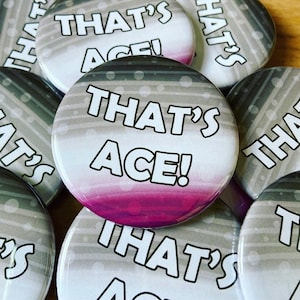 May include: A close-up of several round buttons with a gray and white striped background. The buttons have the text "That's Ace!" in black and white lettering. The button in the center has a pink and purple gradient at the bottom.