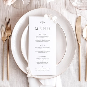 Può includere: Un menu bianco con la parola "MENU" in testo nero. Il menu elenca i seguenti elementi: Antipasto, Piatto principale e Dessert. Gli elementi del menu sono scritti in testo nero su sfondo bianco. Il menu è su una tovaglia bianca con posate d'oro e un piatto bianco.