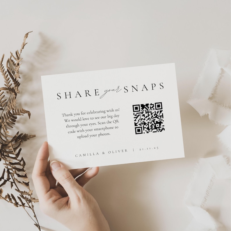 以下が含まれることがあります： 「SHARE your SNAPS」の文字とQRコードが印刷されたクリーム色のカード。イベントの写真の共有をゲストに促すメッセージが記載されています。「CAMILLA & OLIVER」の名前と日付も印刷されています。