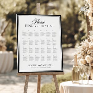 May include: A wedding seating chart on an easel. The black and white sign reads "Please Find Your Seat" and lists names alphabetically. The sign is on a wooden easel, with a champagne bottle and glasses in the foreground.