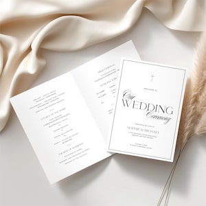 Op de afbeelding: Een wit trouwceremonieprogramma met zwarte tekst, met de woorden "Our Wedding Ceremony" in een decoratief lettertype. Het programma bevat de volgorde van de dienst en een kruissymbool. Het programma is open.