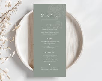 Puede incluir: Una tarjeta de menú verde salvia con detalles florales, que enumera las opciones de entrantes, platos principales y postres. El menú está colocado sobre un plato de madera clara, con flores secas en el fondo. El texto del menú incluye platos como salmón curado con cítricos y panna cotta de vainilla.