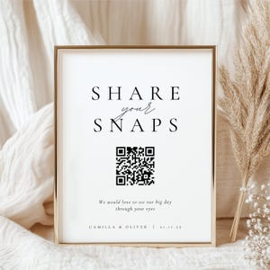 May include: A framed white sign with the text "SHARE your SNAPS" in black. A QR code is below the text, with the words "We would love to see our big day through your eyes" and the names "CAMILLA & OLIVER | 21.11.25" at the bottom.