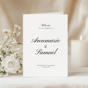 Puede incluir: Una tarjeta de programa de boda blanca con tipografía negra con remates que dice Welcome TO THE WEDDING OF Annmarie & Samuel, Mount Juliet Estate, County Kilkenny, 9th August 2026. La tarjeta se muestra en posición vertical sobre una superficie.