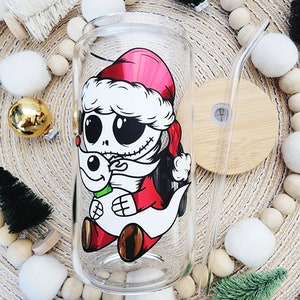 May include: A clear glass tumbler with a festive design featuring Jack Skellington from The Nightmare Before Christmas wearing a Santa hat and holding Zero. The tumbler has a red and white Santa hat design and a straw.