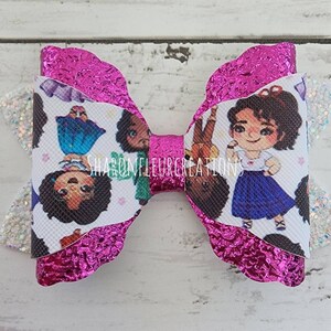 May include: A pink glitter hair bow with a white fabric featuring a repeated pattern of cartoon characters. The characters are all wearing colorful outfits and have brown skin and dark hair. The bow is tied in a classic shape with a scalloped edge.