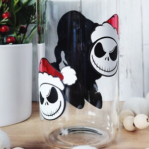 May include: A clear glass tumbler with a black and white image of Jack Skellington from The Nightmare Before Christmas wearing a Santa hat. The image is repeated twice on the glass.