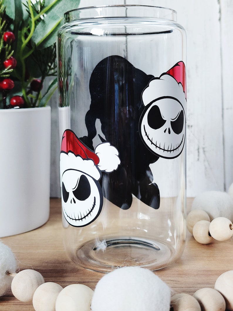 May include: A clear glass tumbler with a black and white image of Jack Skellington from The Nightmare Before Christmas wearing a Santa hat. The image is repeated twice on the glass.