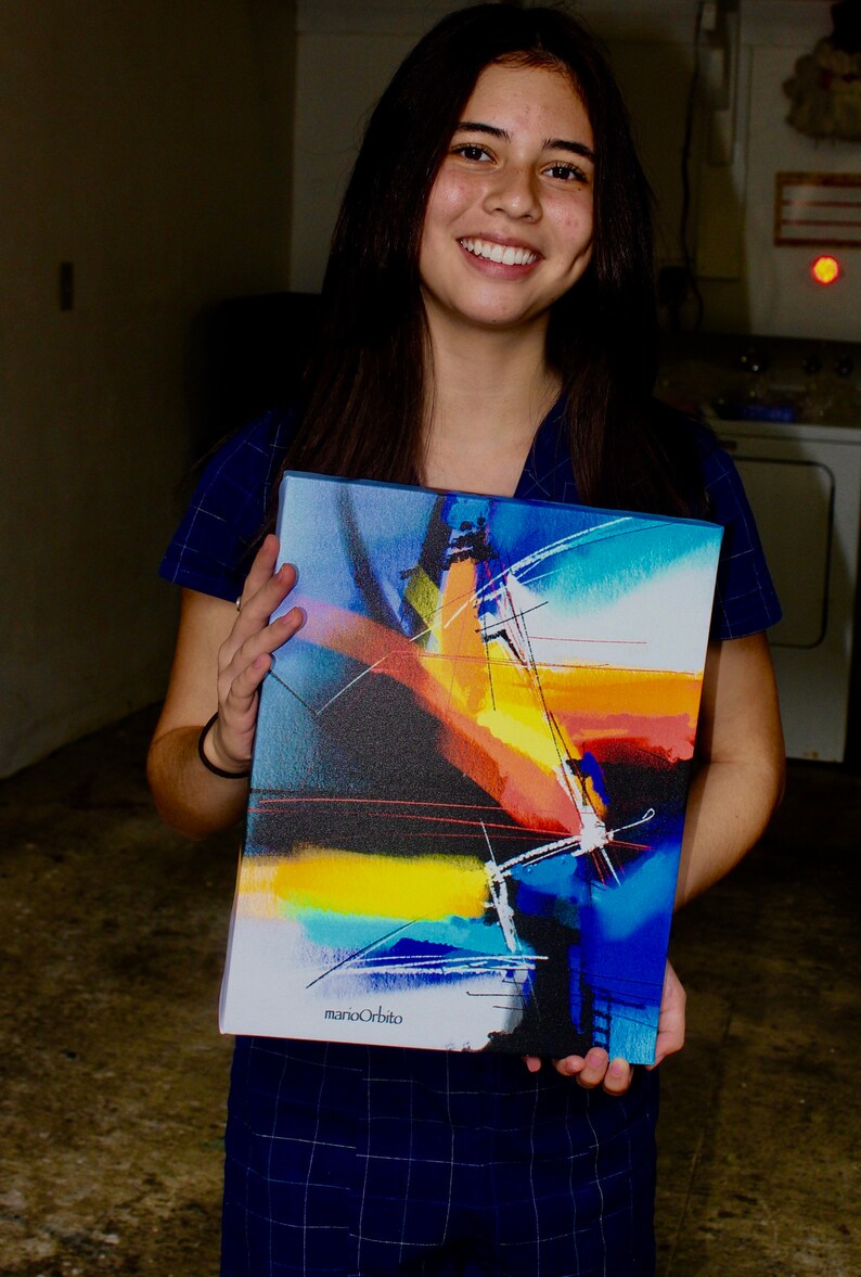 May include: A young person holding a colorful abstract painting with a black, yellow, orange, blue, and white color scheme. The painting is signed "marioOrbito" in the bottom right corner.