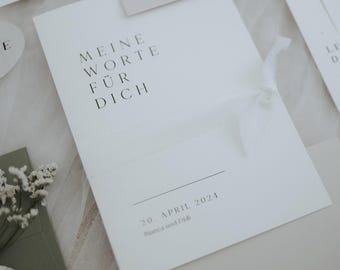 Könnte beinhalten: Eine weiße Einladungskarte mit dem Text "MEINE WORTE FÜR DICH" in Schwarz. Die Karte ist mit einem weißen Band gebunden und enthält das Datum "20. APRIL 2024" und Namen. Weitere Karten sind im Hintergrund sichtbar.