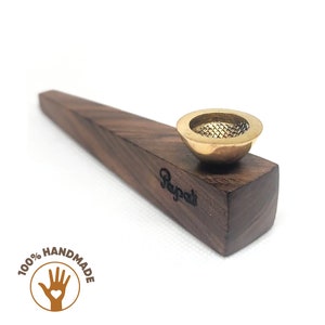 Puede incluir: Una pipa de fumar de madera con una cazoleta de latón y una rejilla. La pipa está hecha de madera oscura y tiene una forma rectangular. La cazoleta es redonda y tiene un pequeño agujero en el centro. La pipa está grabada con la palabra "Raypati".