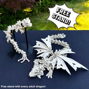 May include: Two white skeletal dragon figurines, one with wings spread and the other curled up. The larger dragon is on a black stand. The text "FREE STAND!" is in a speech bubble above the dragons.