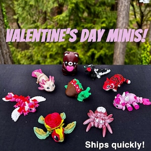 May include: Valentine's Day Minis! A collection of nine small, hand-painted figurines, including a bear holding a heart, a strawberry, a turtle, a spider, a unicorn, a fish, a skunk, a dragon, and a lobster.