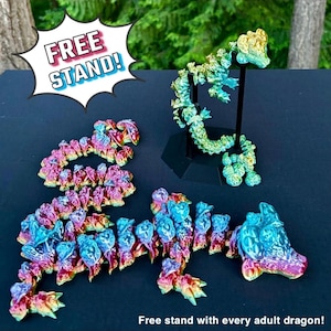 May include: A set of iridescent, multi-colored, plastic dragon figurines. The dragons are arranged in a curled, serpentine shape. The text "FREE STAND!" is in a speech bubble in the upper left corner of the image.