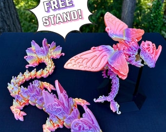 May include: Three 3D printed dragon figurines with intricate details. The dragons are pink, purple, and gold with a butterfly wing design. The dragons are on a black surface with a sign that says "FREE STAND!"  Free stand with every adult dragon.