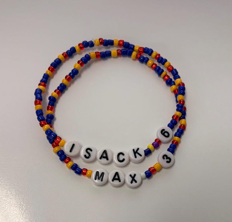 May include: Two circular beaded bracelets featuring a repeating pattern of small blue, yellow, and red glass beads. One bracelet includes white round letter beads spelling ISACK and the number 6. The other bracelet features white letter beads spelling MAX and the number 3.