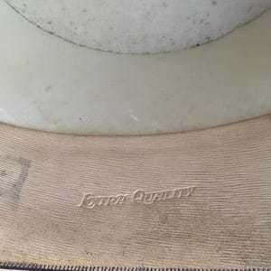 May include: Interior view of a vintage hat. The hat's interior features a cream-colored lining and a tan band with the embossed text "Extra Quality". The hat's brim is visible at the bottom.