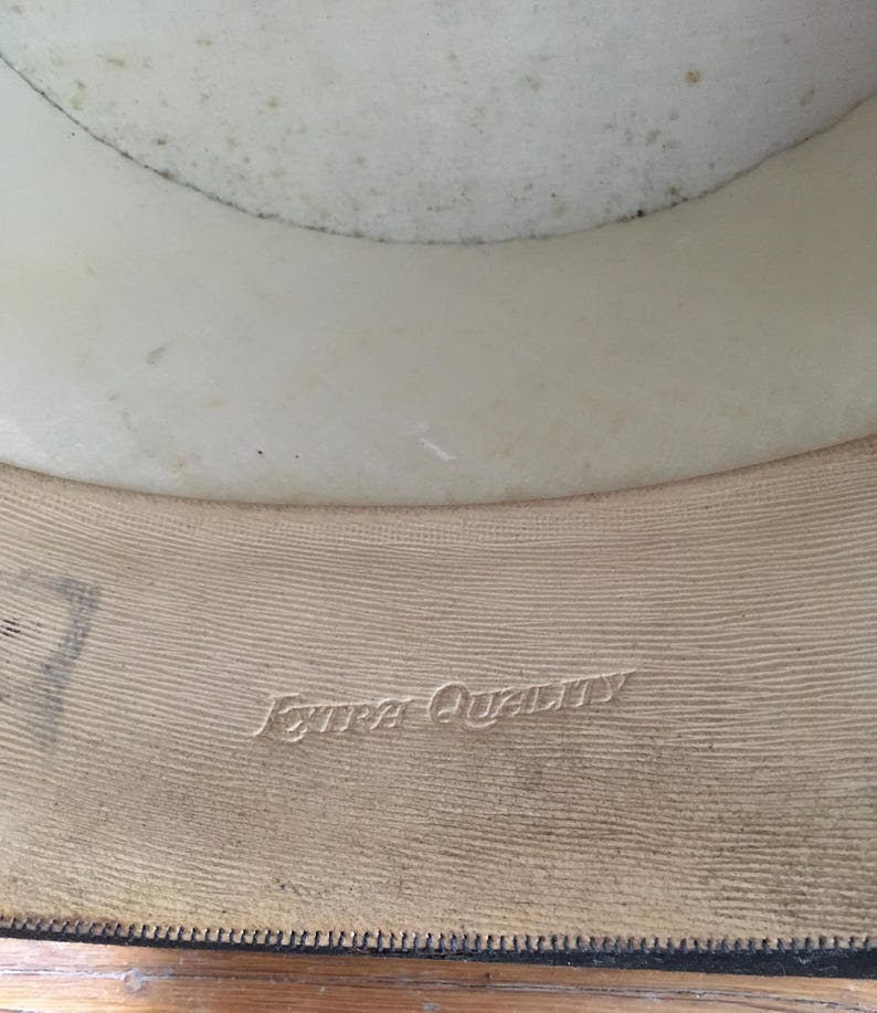 May include: Interior view of a vintage hat. The hat's interior features a cream-colored lining and a tan band with the embossed text "Extra Quality". The hat's brim is visible at the bottom.