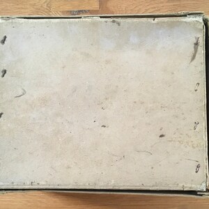 May include: An open, rectangular cardboard box with a light brown lid. The lid is secured with small metal staples. The box is sitting on a wooden surface.