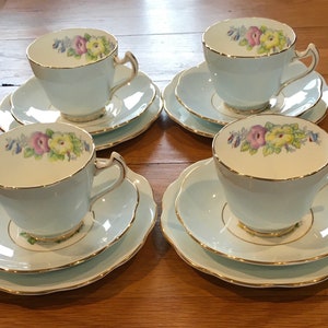 Könnte beinhalten: Ein Set aus vier hellblauen Teetassen und Untertassen mit Blumendesigns. Jede Tasse und Untertasse hat einen zarten goldenen Rand.