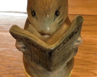 May include: A ceramic figurine of a mouse reading a newspaper. The mouse is brown with black eyes and is holding a newspaper with the word "Gawlor" visible. The mouse is sitting on a yellow spool of thread with a red thread wrapped around it.