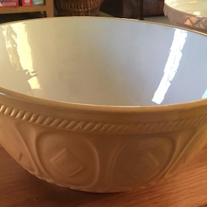May include: A large, beige ceramic mixing bowl with a white interior. The bowl has a decorative, raised design around the rim and sides.